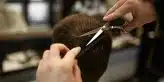 a person cutting another persons hair with a pair of scissors