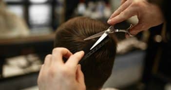 a person cutting another persons hair with a pair of scissors